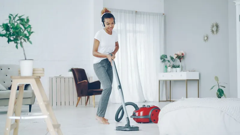 A woman in a cozy room uses a vacuum cleaner while enjoying music on headphones