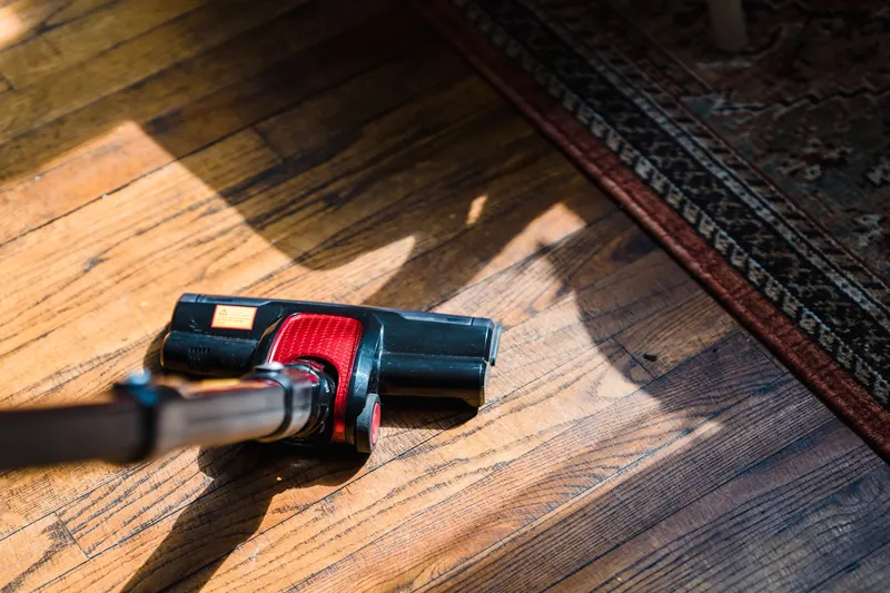 Close-up of a vacuum cleaner on wooden flooring near a patterned rug, showcasing domestic cleaning