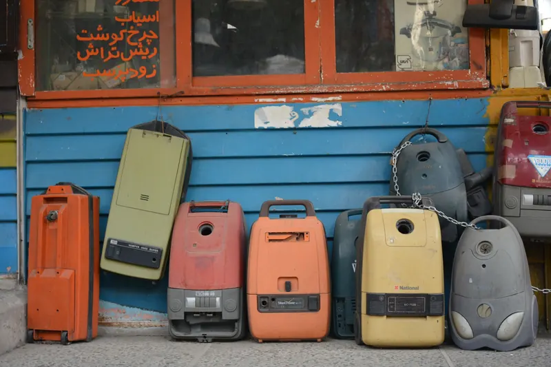 A row of colorful vintage vacuum cleaners displayed against a blue wall in Tehran, Iran