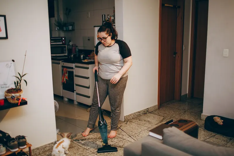 A woman cleaning her living room with a vacuum cleaner while her pet rabbit watches