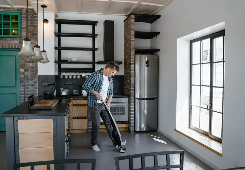A man cleaning the modern kitchen with a vacuum cleaner, showcasing contemporary interior design