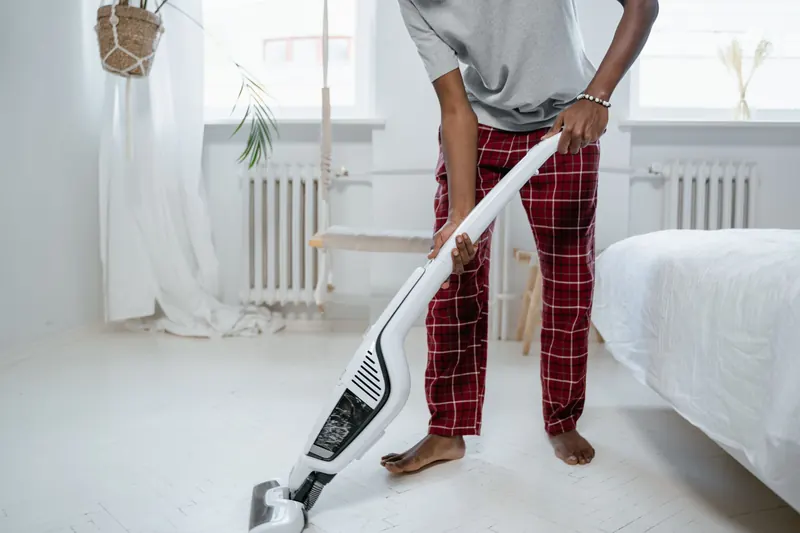 A person cleaning a bedroom with a modern vacuum cleaner, showcasing casual home lifestyle