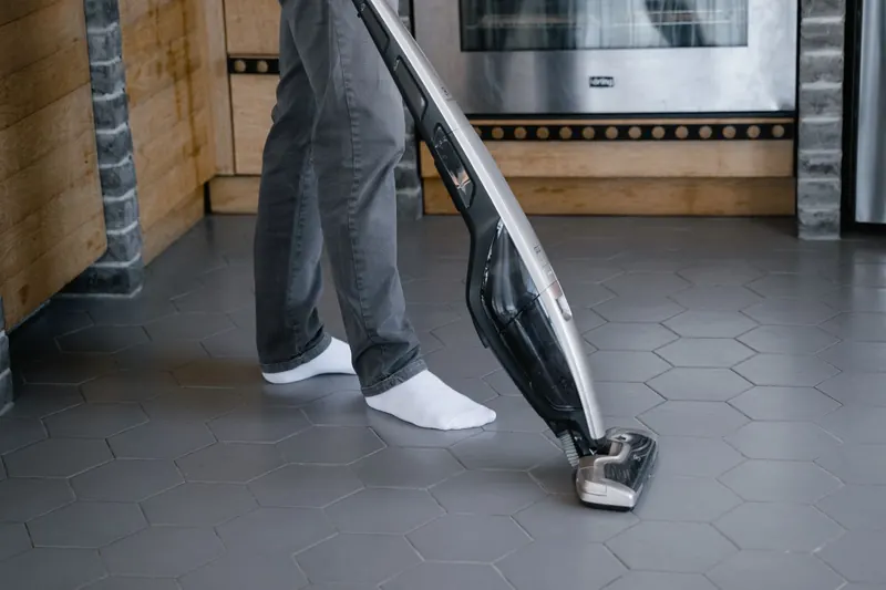 A person cleaning a tiled floor with a modern vacuum cleaner indoors