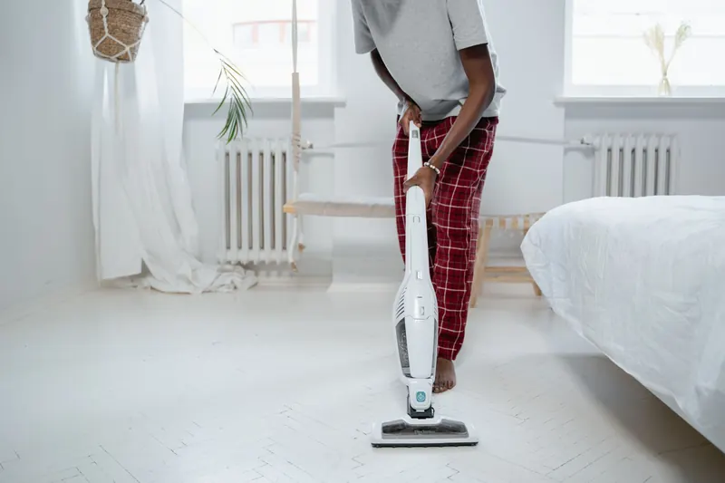 Man cleaning a room with a vacuum cleaner, barefoot in pajamas, ensures tidiness