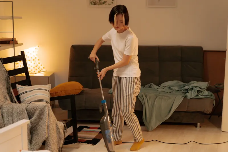 Asian woman cleaning a messy living room at home with a vacuum cleaner, creating a tidy space
